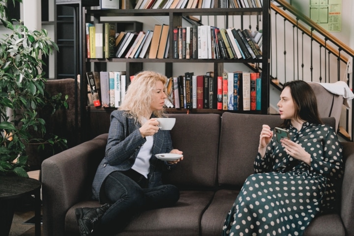 Twee vrouwen zitten samen op de zetel met een kop thee in de hand. Ze praten met elkaar.
